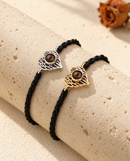 Silberfarbenes und goldfarbenes Engelsflügel-Herz-Armband nebeneinander auf einem Travertinblock