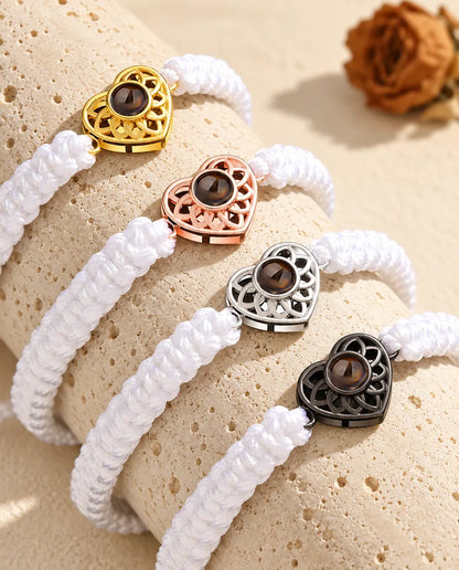 Vier Armbänder mit weissem Flechtband und Herz in Gold, Roségold, Silber und Schwarz auf Travertin