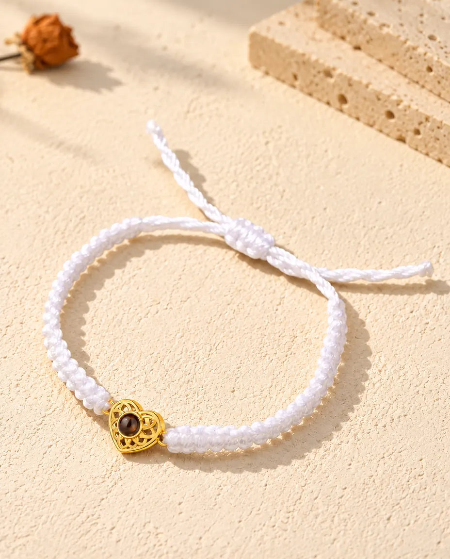 Armband mit weissem Flechtband, goldfarbenem Herz und Schiebeknoten auf hellem Gips
