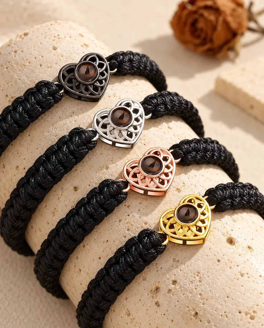 Vier Armbänder mit schwarzem Flechtband und Herz in allen Charm-Farben über einem Travertinblock