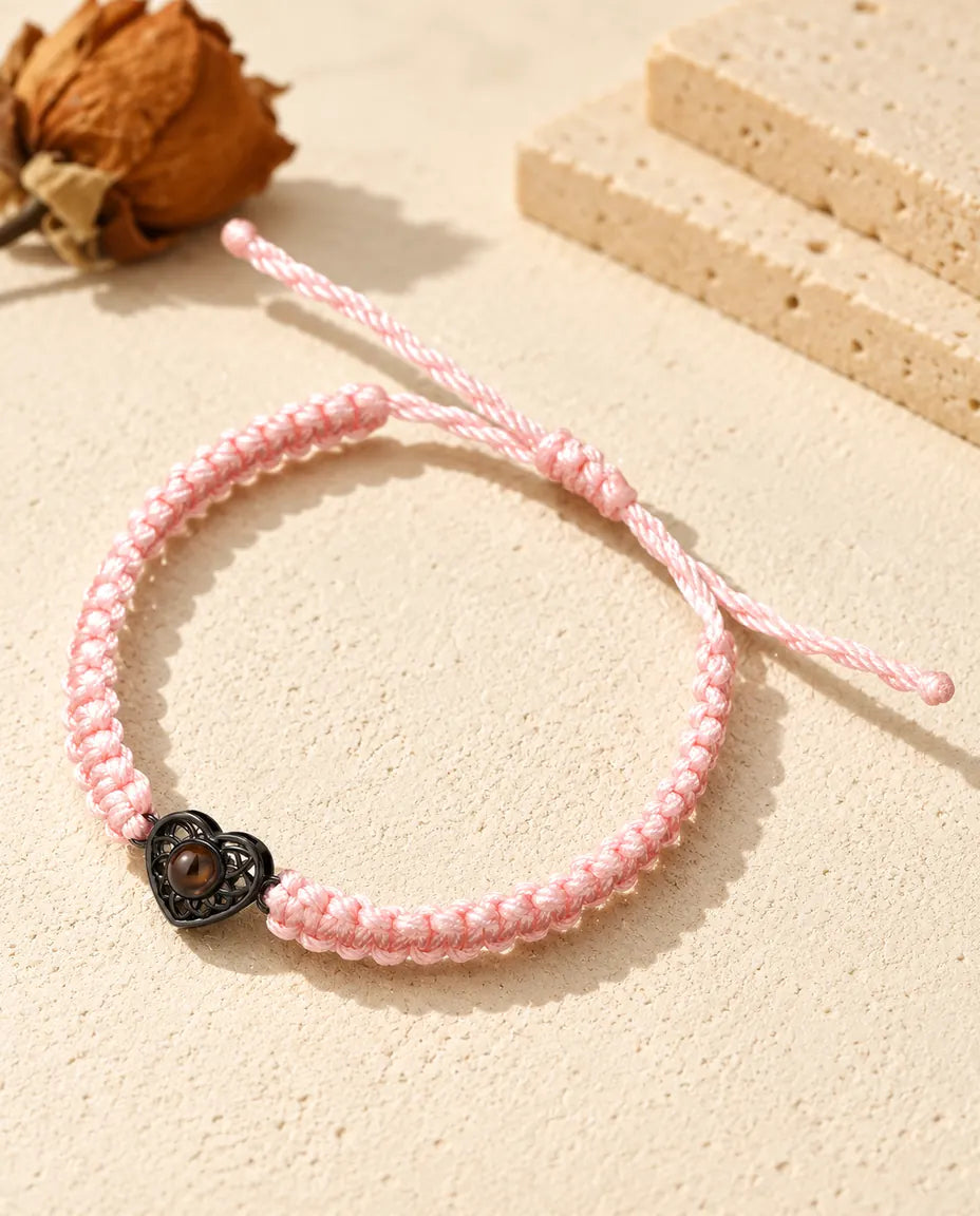 Armband mit rosa Flechtband, schwarzem Herz und braunem Bildstein auf hellem Gips