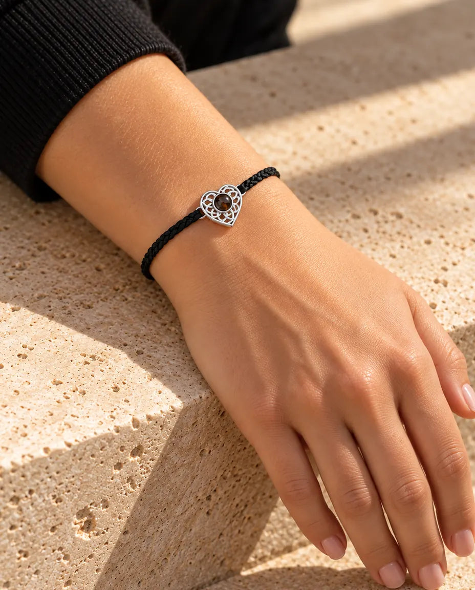 Frau trägt das Armband mit schmalem schwarzem Flechtband und silberfarbenem Herz am Handgelenk im Sonnenlicht