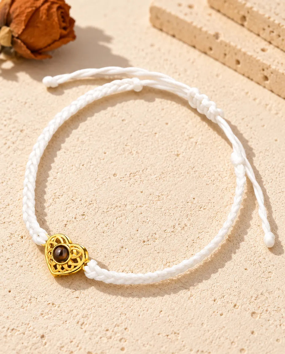 Armband mit schmalem weissem Flechtband, goldfarbenem Herz und Schiebeknoten auf hellem Gips