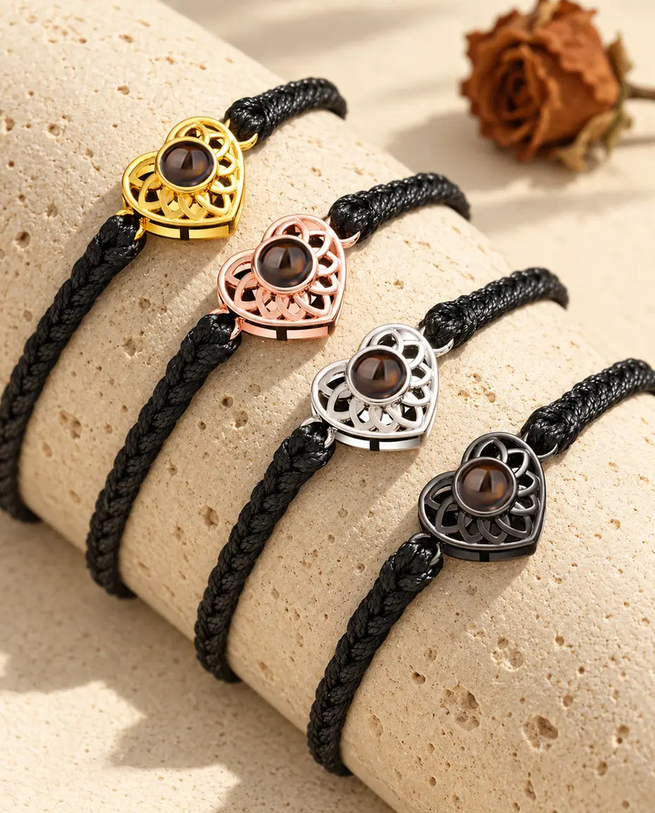 Vier Armbänder mit schmalem schwarzem Flechtband und Herz in allen Charm-Farben über einem Travertinblock
