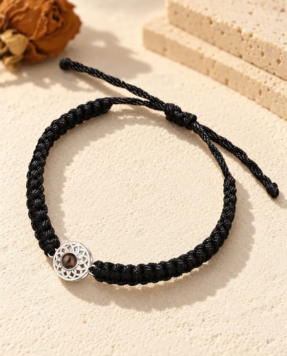 Armband mit Bild im Stein: silberfarbener durchbrochener Rund-Charm an schwarzem Flechtband auf hellem Gips