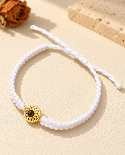 Armband mit weissem Flechtband, goldfarbenem Rund-Charm und Schiebeknoten auf hellem Gips