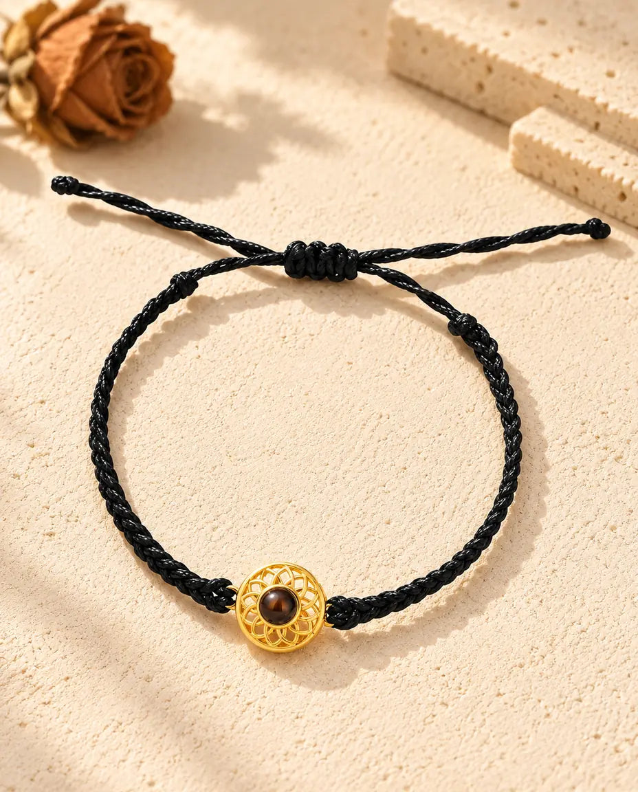 Draufsicht: Armband mit goldfarbenem Rund-Charm an schmalem schwarzem Flechtband, mit Schiebeknoten und Bandenden