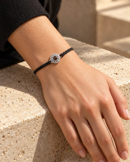 Frau trägt das Armband mit schmalem schwarzem Flechtband und silberfarbenem Rund-Charm am Handgelenk im Sonnenlicht