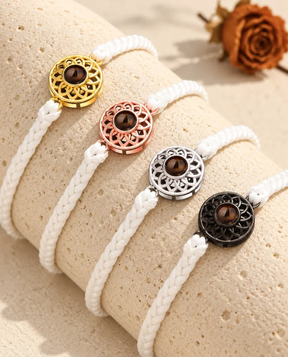 Vier Armbänder mit schmalem weissem Flechtband und Rund-Charm in Gold, Roségold, Silber und Schwarz auf Travertin