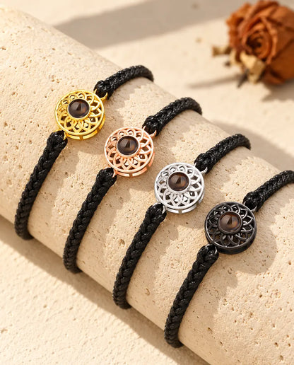Vier Armbänder mit schmalem schwarzem Flechtband und Rund-Charm in allen Charm-Farben über einem Travertinblock