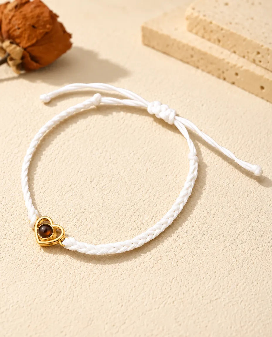 Armband mit weissem Flechtband, goldfarbenem offenem Herz und Schiebeknoten auf hellem Gips