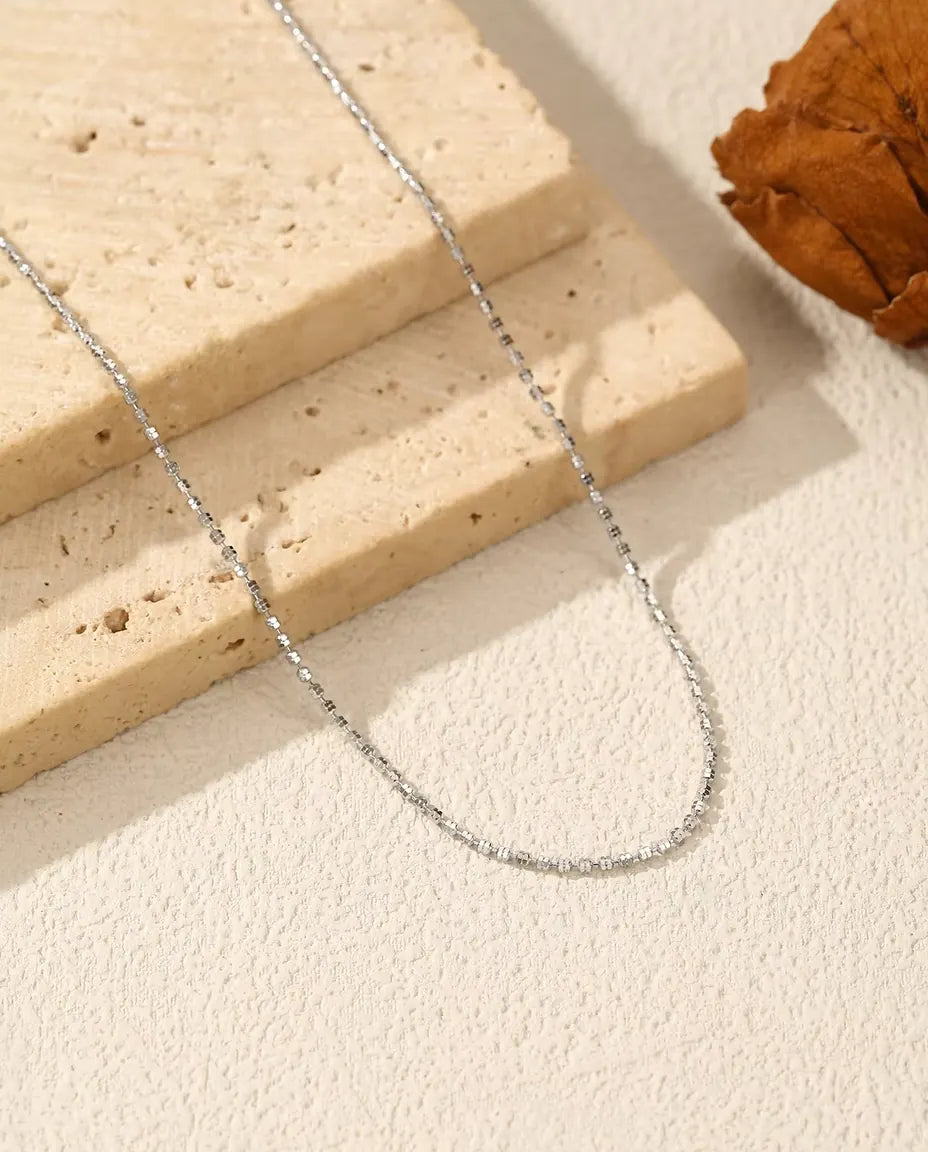 Funkelnde Kette aus 925 Sterlingsilber - über helle Fläche neben einer Travertinplatte gelegt
