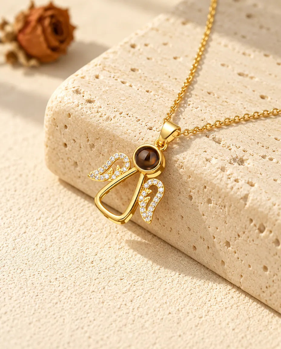 Goldfarbene Schutzengel-Kette mit Zirkonia-Flügeln auf Travertin