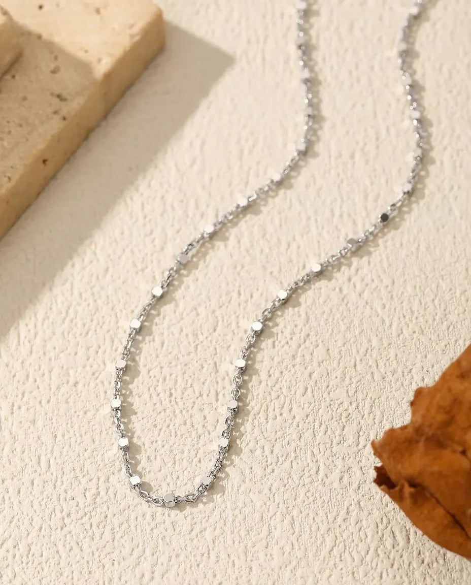 Plättchen Kette aus 925 Sterlingsilber - über helle Fläche neben einer Travertinplatte gelegt