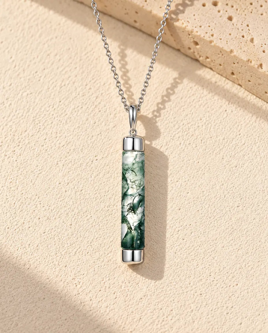 Moosachat Kette mit langem Zylinder aus 925 Sterlingsilber - auf heller Strukturfläche neben einem Travertinblock liegend