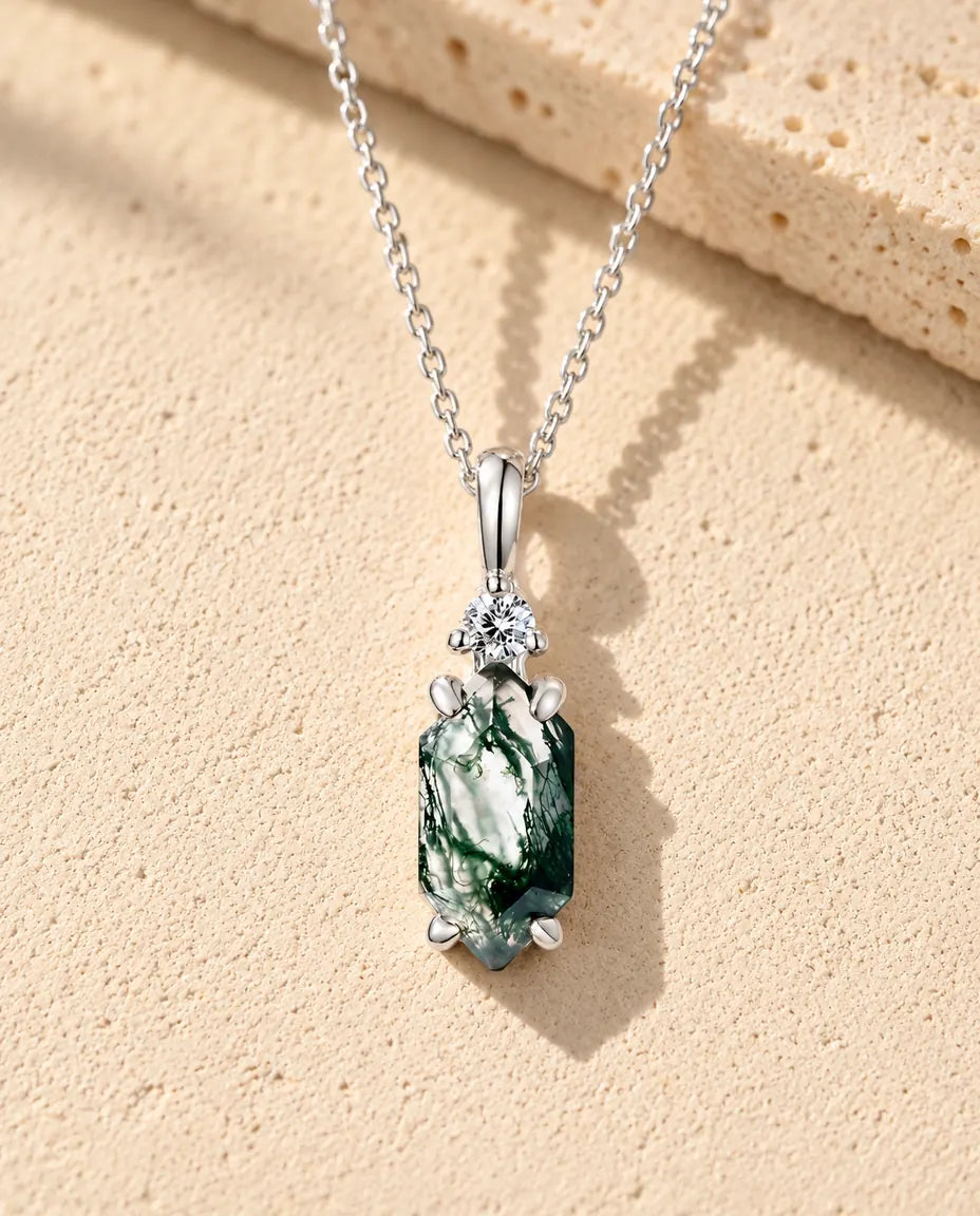 Moosachat Kette mit schmalem Sechseck aus 925 Sterlingsilber - auf heller Strukturfläche neben einem Travertinblock liegend