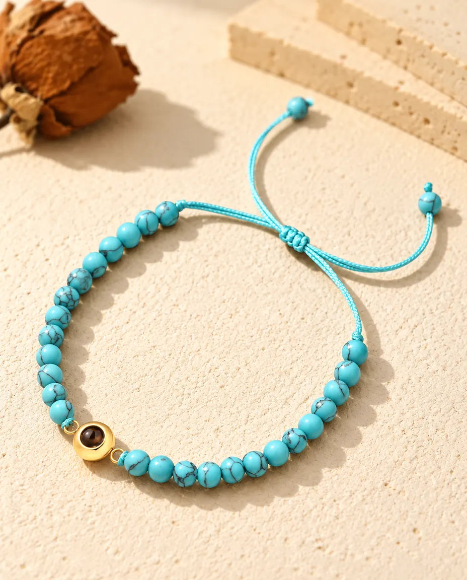 Personalisiertes Perlenarmband mit Bild im Stein: blau marmorierte Perlen und goldfarbener Ring-Charm auf Gips