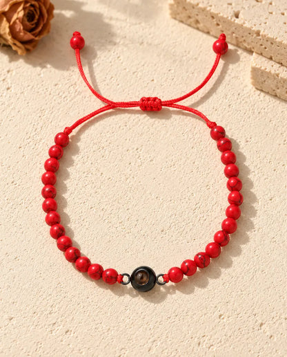 Draufsicht: rotes Perlenarmband mit schwarzem Ring-Charm und Schiebeknoten