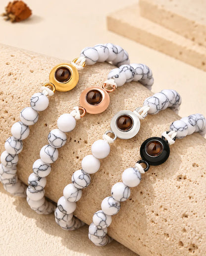 Weiss marmorierte Perlenarmbänder in jeder Charm-Farbe über einem Travertinblock