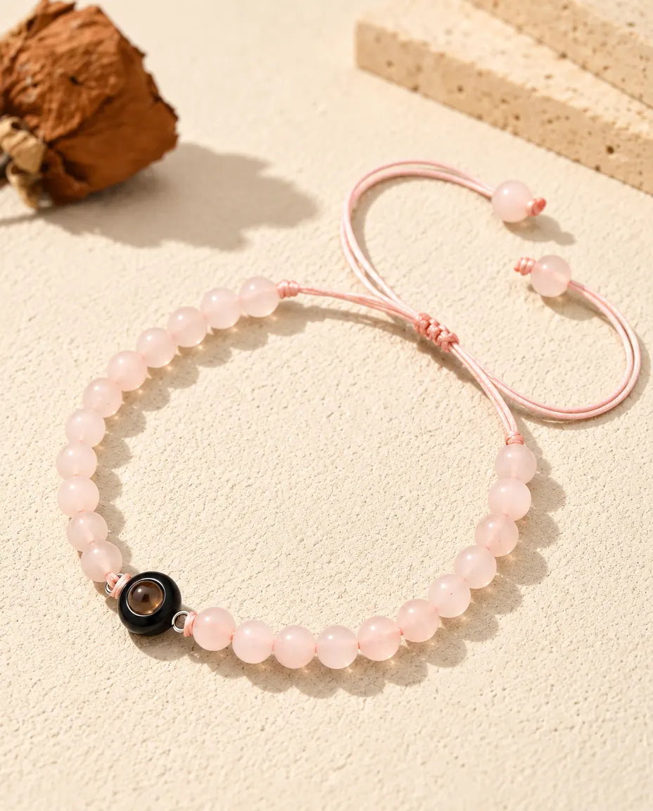 Zartrosa Perlenarmband mit schwarzem Ring-Charm auf hellem Gips