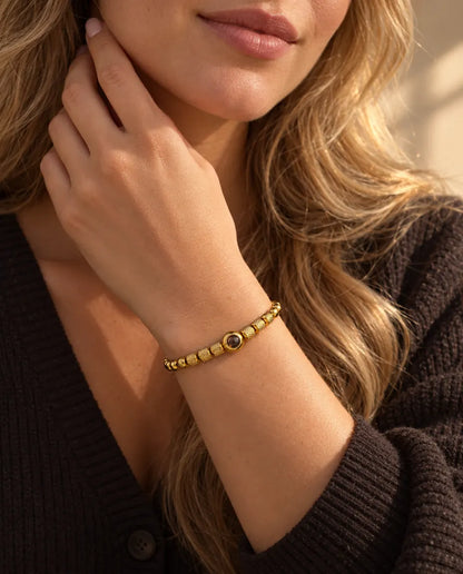 Frau berührt ihren Hals und trägt das goldfarbene Armband mit strukturierten Perlen und Bild im Stein