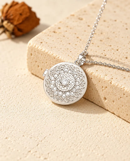 Silberfarbenes rundes Foto-Medaillon mit Mandala-Blume als personalisierte Kette, an einen Travertinblock gelehnt